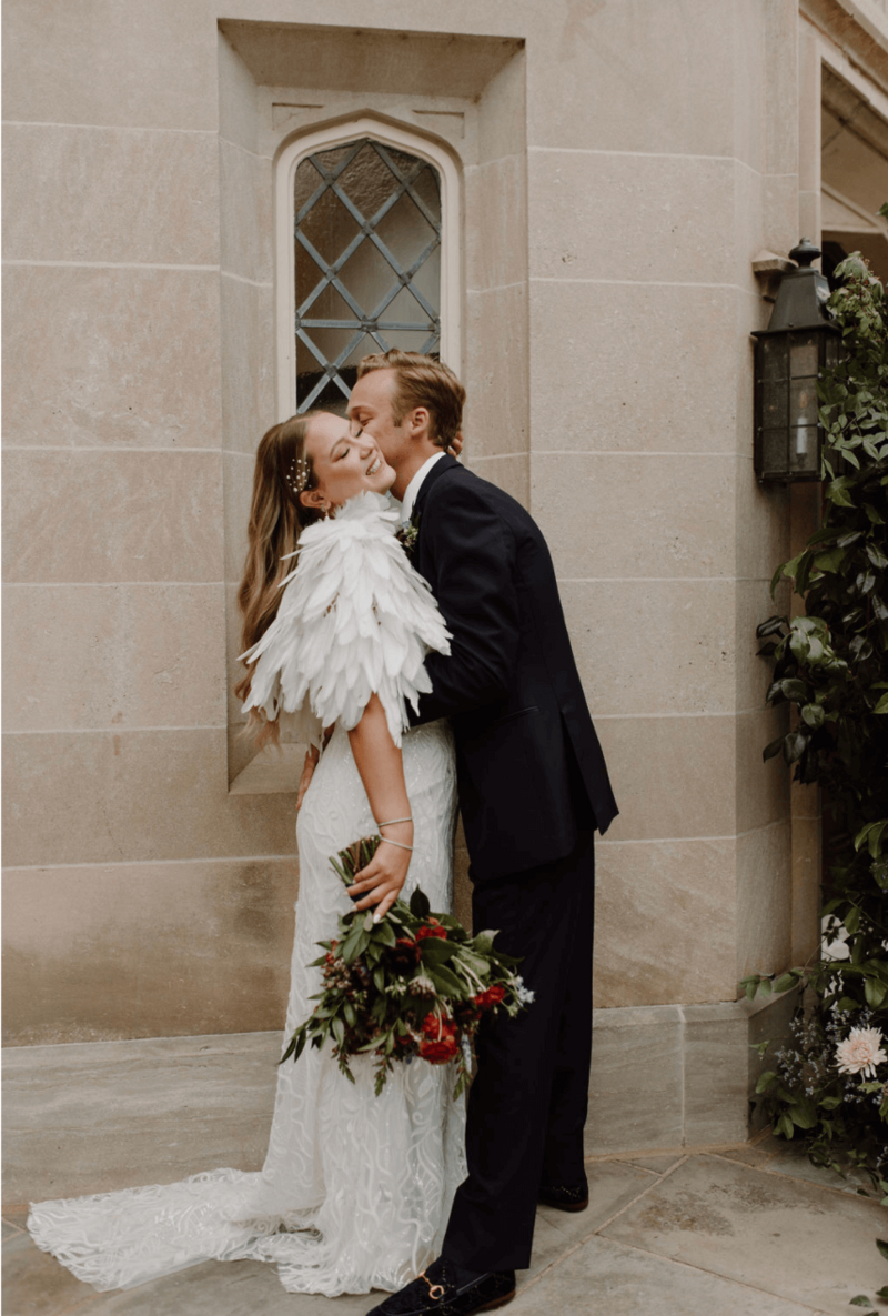 The groom kisses the bride on the cheek, she embraces him, and smiles.