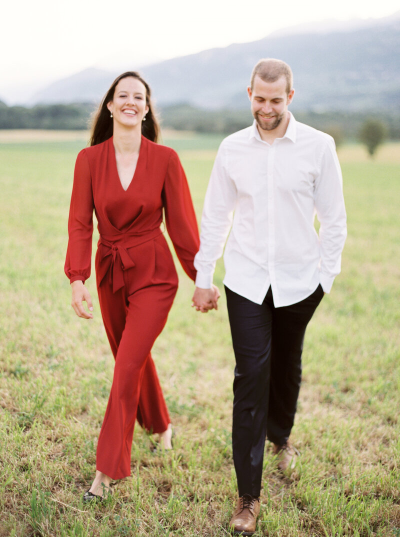 Woman and man smile while walking hand in hand through field
