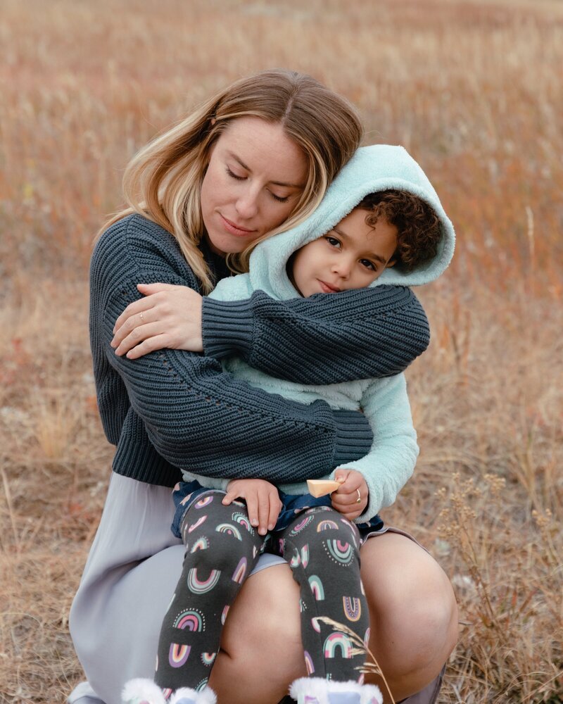 An outdoor family portrait featuring a mother warmly embracing her son. The natural setting highlights the tender bond between them, capturing a moment of affection and connection in a beautiful outdoor environment.