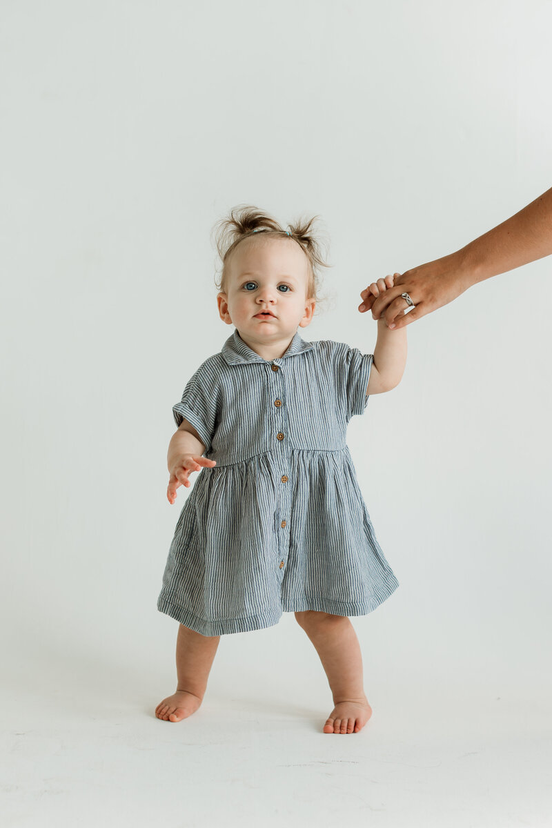 Mom letting her 1 year old daughter hold her hand as daughter stands