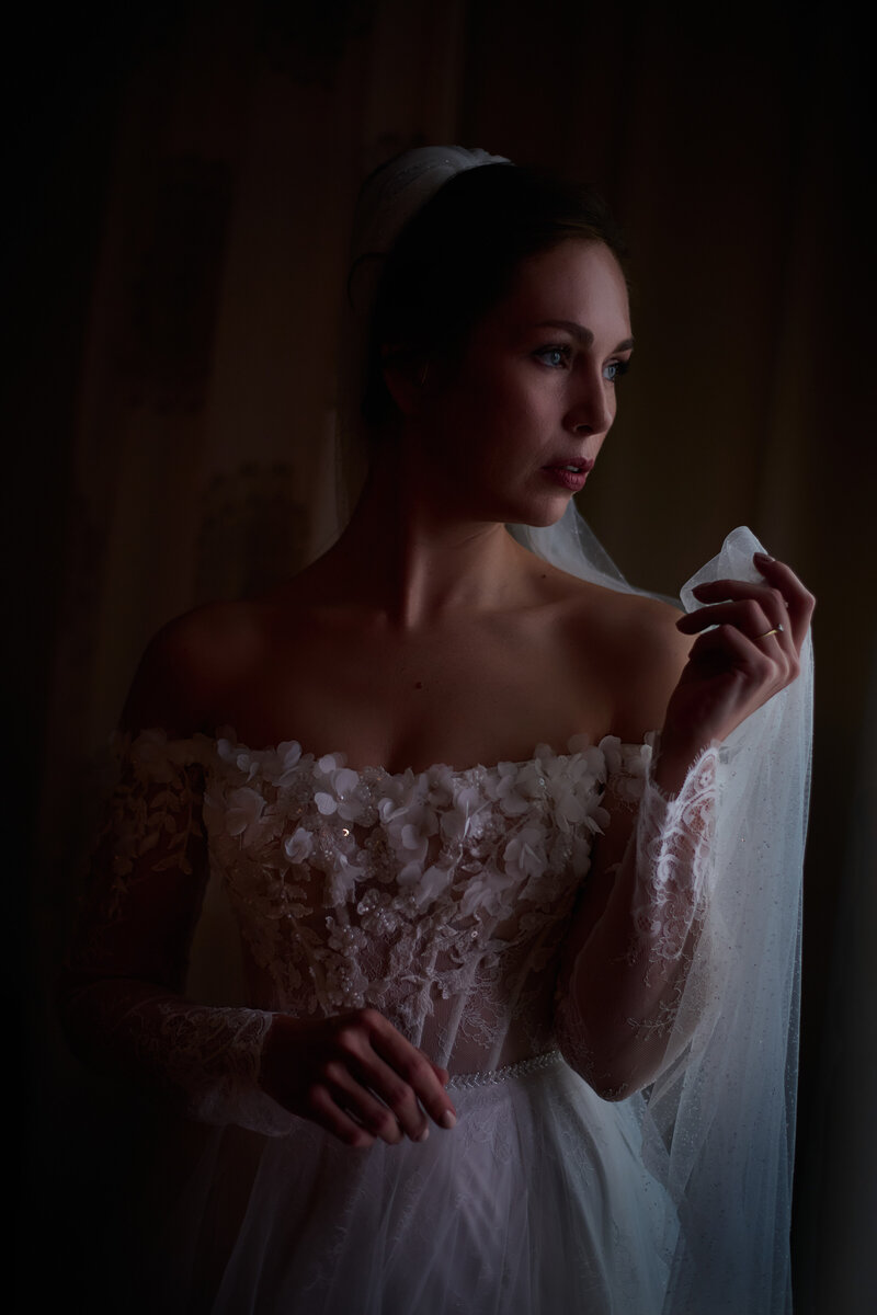 Braut steht am Fenster und hält ihren Schleier. Hotel Ingolstadt Getting Ready Hochzeit