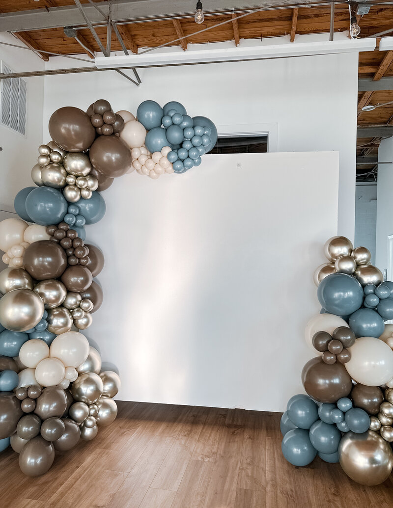 Blue, brown and gold organic balloon garland on white wall for baby shower.