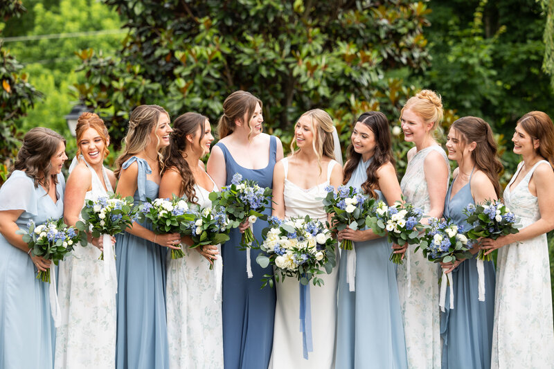 Spring wedding at WinMock at Kinderton, designed by Charming Carolina — bride and bridesmaids posing with dusty blue and greenery bouquets outside the venue’s barn.