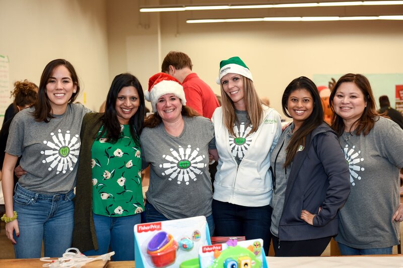 A group of cheerful volunteers wearing festive outfits and Santa hats posing for a photo during a holiday charity event