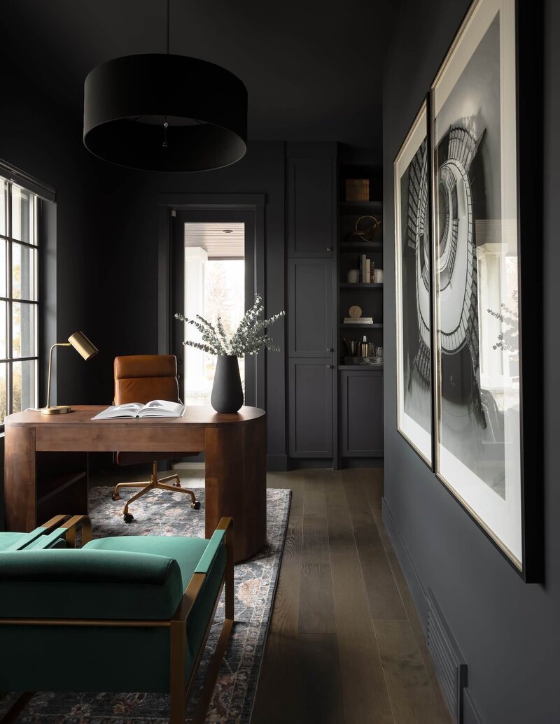 A modern moody dark home office paired with walnut features and emerald green accents chairs.