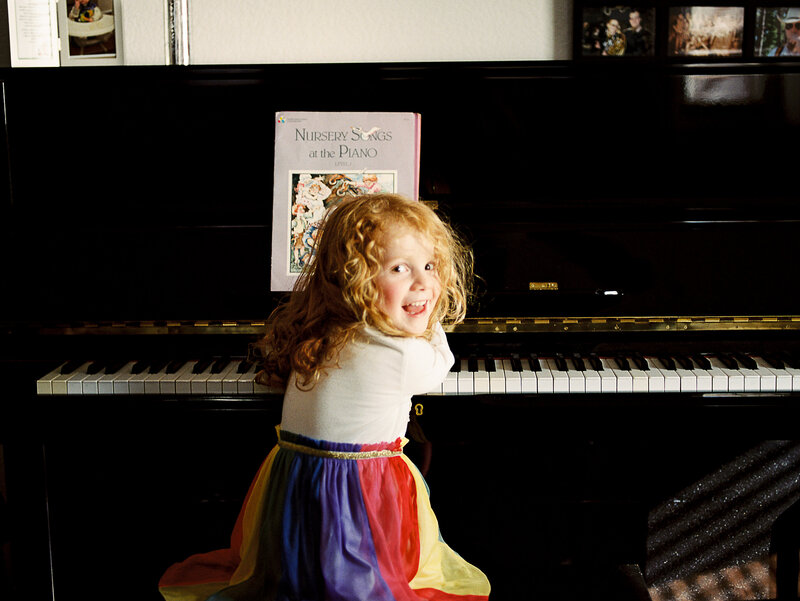 girl with red curls looks back at camera while playing piano