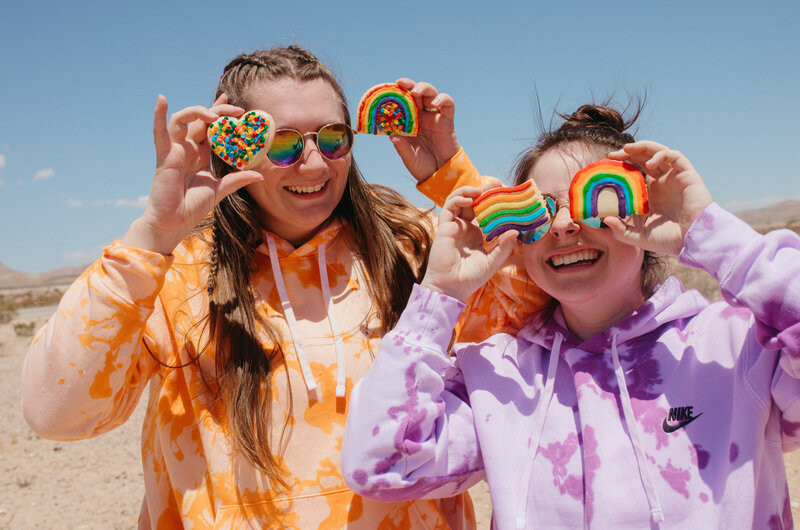 two friends joke around holding rainbow cookies