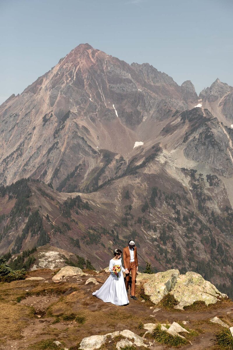 A wedding couple walking on a ridge with a big mountain behind in the North Cascades