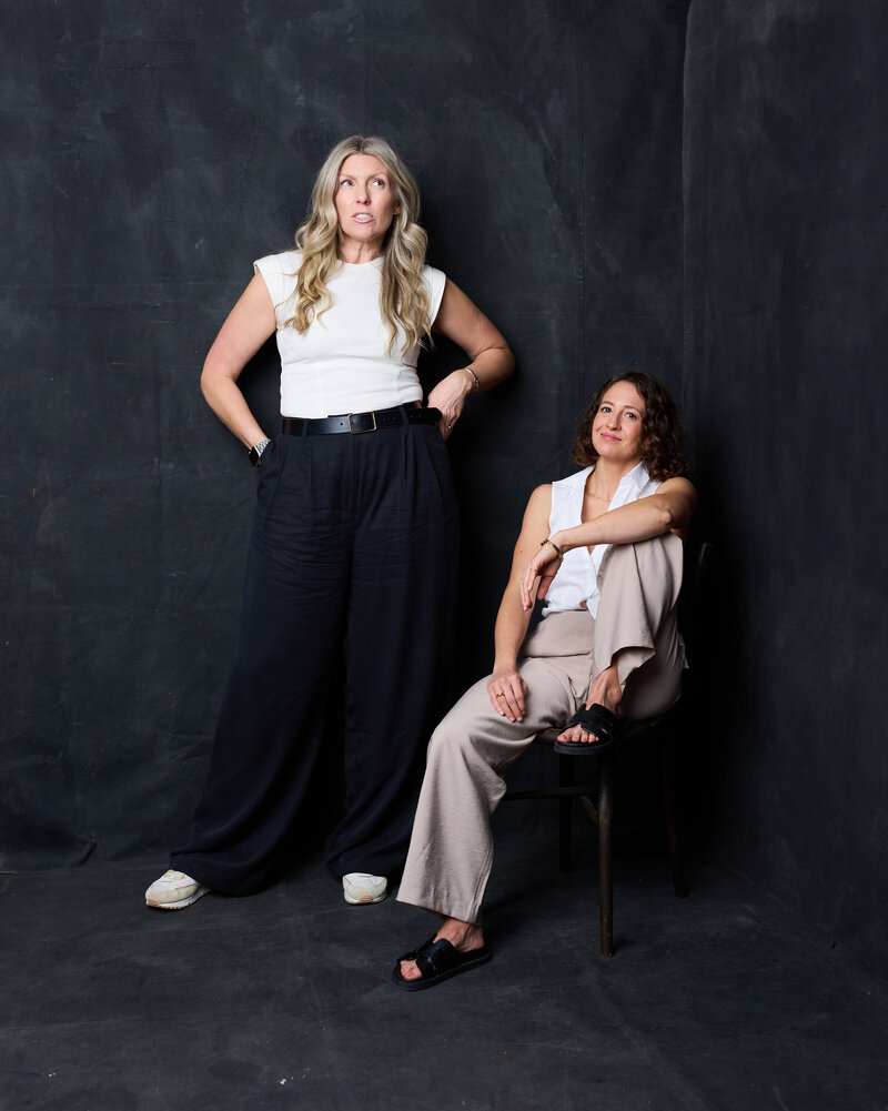 Studio portrait of UN(COMMON) co-founders Kate and Justine against a dark, dramatic background.