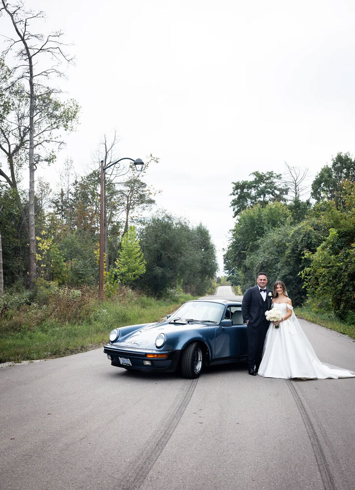 couple posing on wedding day with car