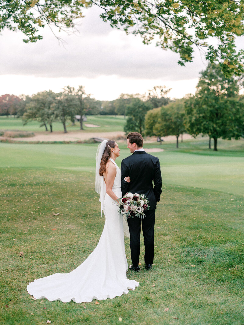 Bride and groom looking at each other standing on a green hill overlooking a gold course