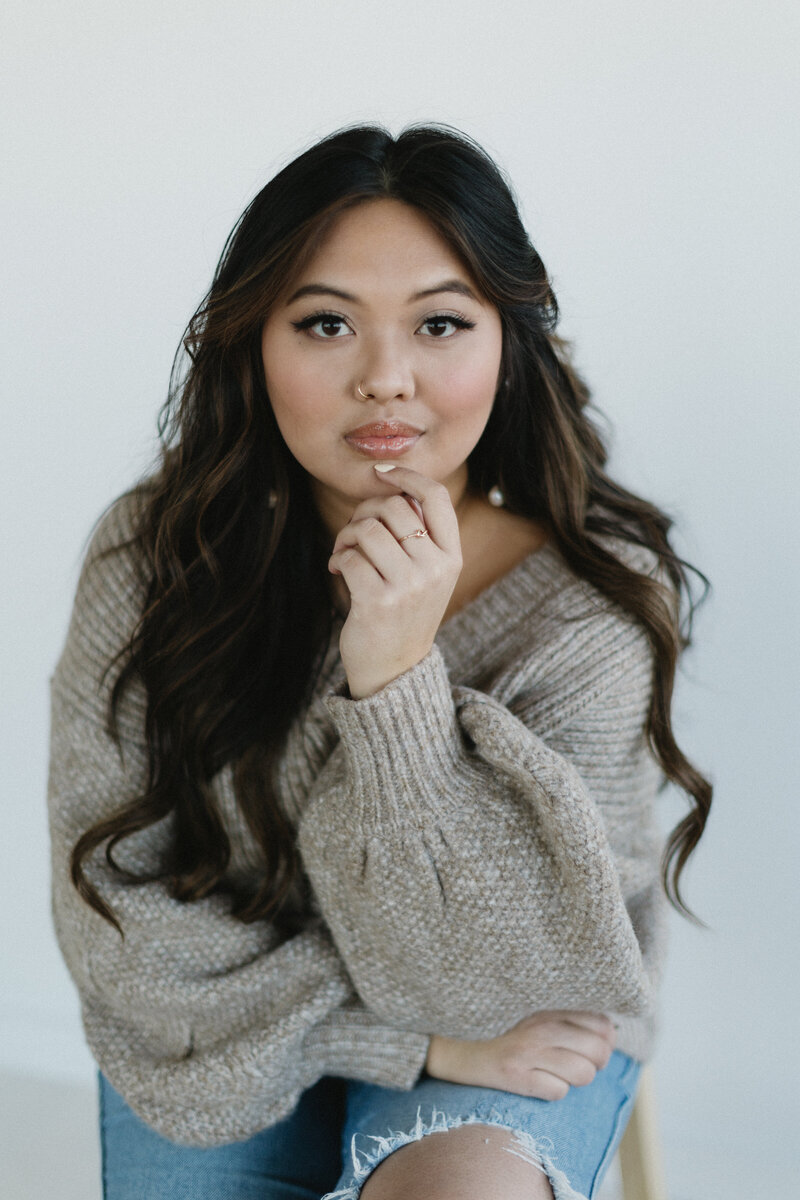 Portrait of an Asian American woman with long hair, resting her hand on her chin, showcasing natural beauty and confidence in a personal branding shoot.