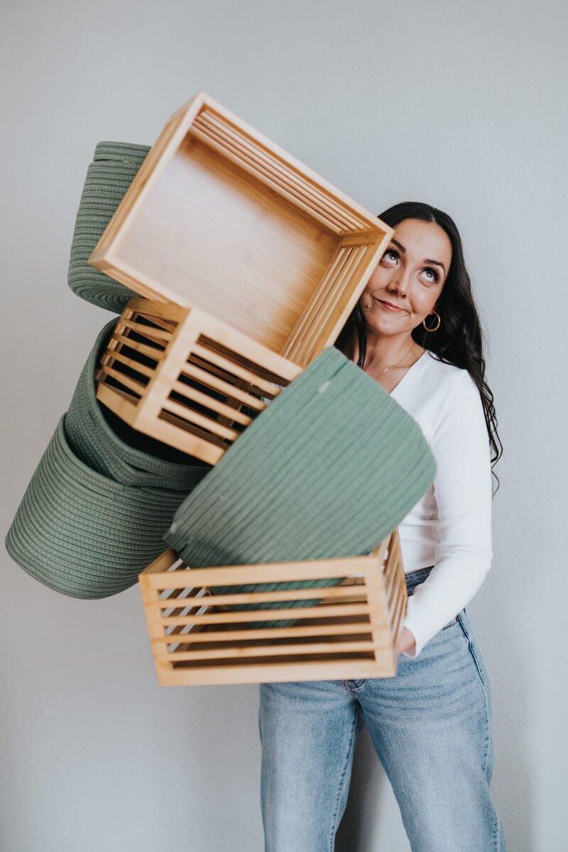 Woman wearing white, long-sleeve t-shirt balances several organizational boxes and bins.