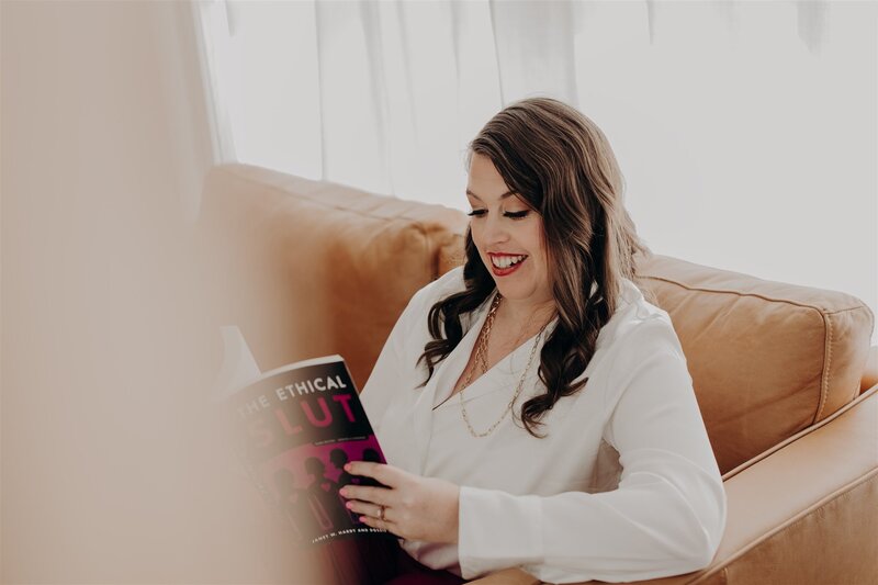 woman in white shirt looking down into book while sitting on a brown leather couch