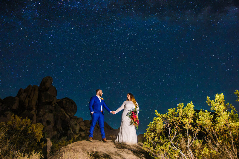 bride and groom standing on rock with starry night sky