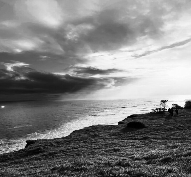 black and white photo of ocean and clouds taken from the shore