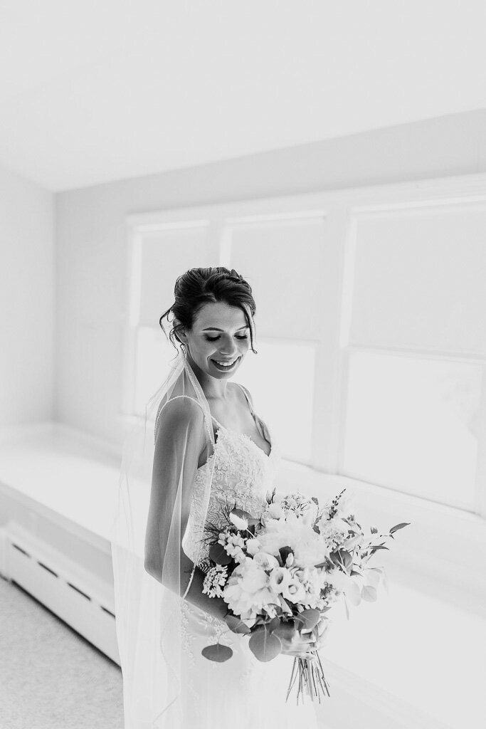 Bridal portrait with a wedding bouquet by the window, capturing a graceful tilt of her head and a radiant smile.
