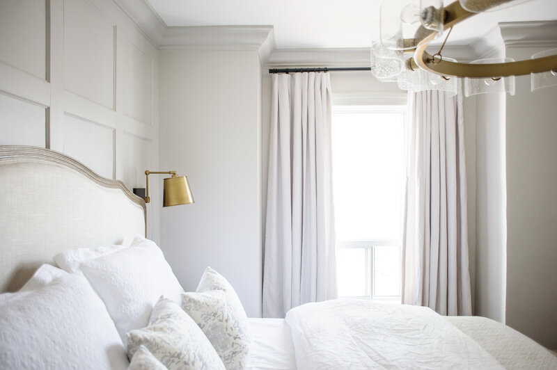 grey and white bedroom with applied wall panelling and crisp white bedding with gold light fixtures