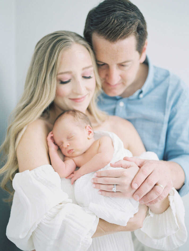 Father leans into his blonde wife as she holds their newborn baby photographed by Newborn Photographer Baltimore Marie Elizabeth Photography