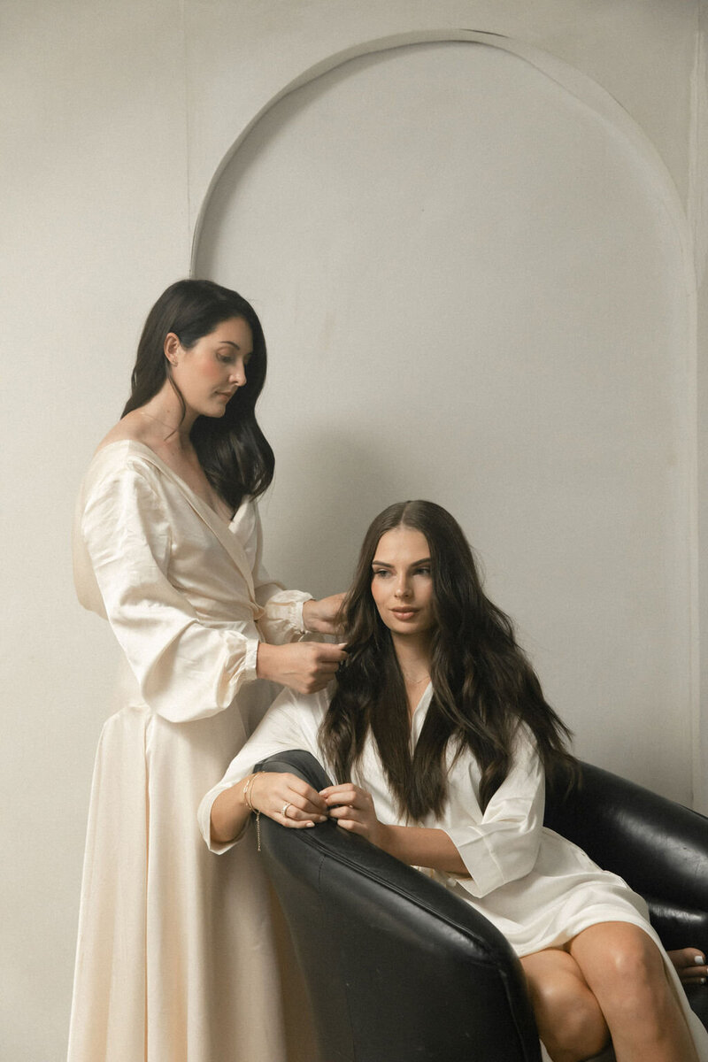 Bridal hairstylist styling a bride's hair while she wears a white robe