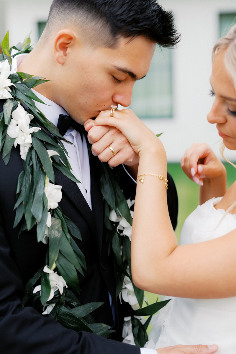 Groom kisses bride’s hand during an emotional moment at their Nichols Heir wedding in Tennessee, wearing a traditional lei and classic black tux.