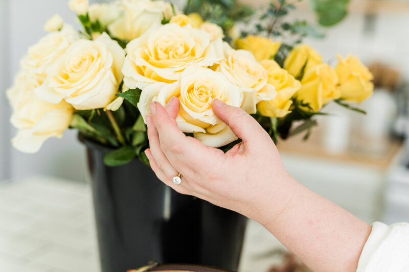 Brand detail image of a florist selecting a yellow rose from a bucket of fresh flowers to cut