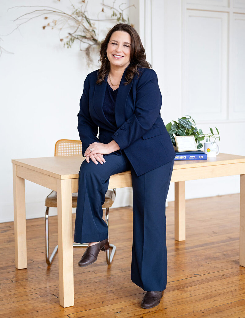 Chris smiling and talking with a client while sitting on a white couch, wearing a blue blazer.