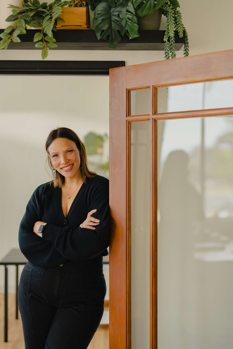 Emily Marson smiling and leaning against a door inviting your into the acupuncture clinic