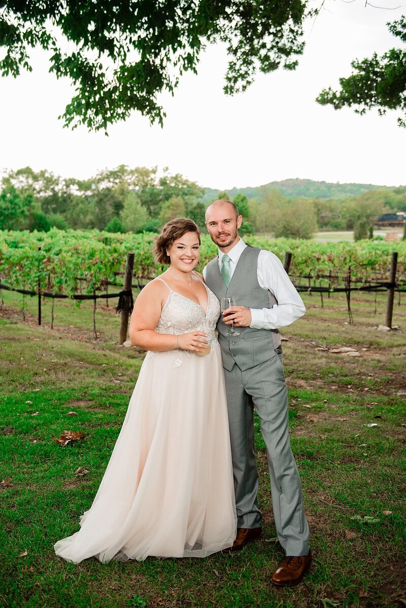 Bride and groom holding glasses of wine standing in the vineyards at their venue
