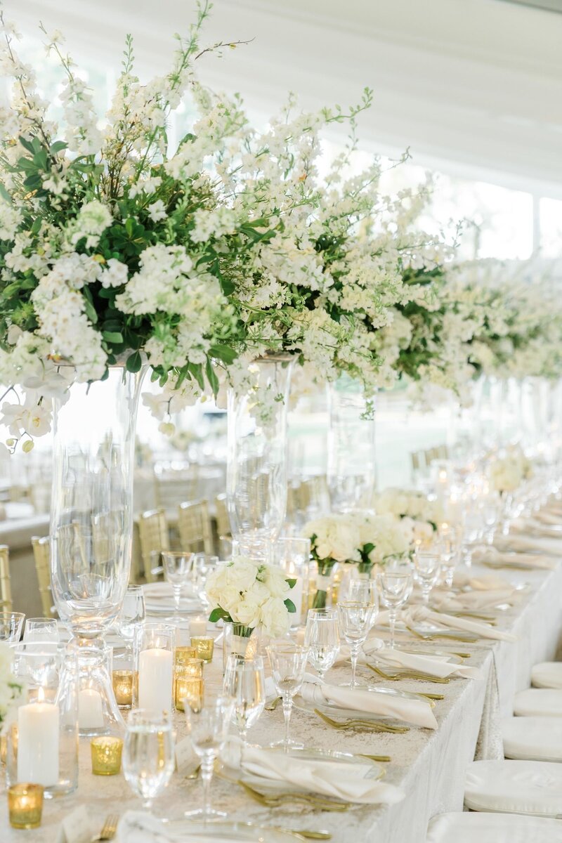 Elegant reception tables decorated with floral arrangements, table settings, and numerous candles