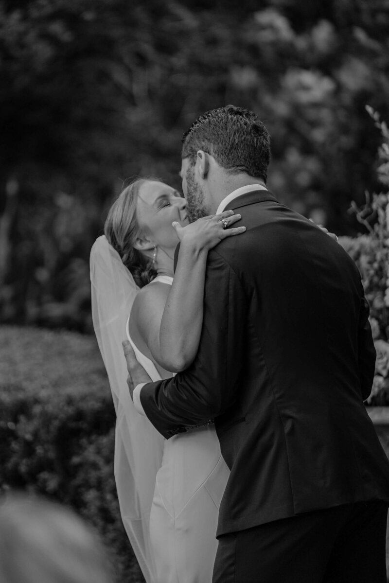 black and white photo of bride and groom kissing during ceremony