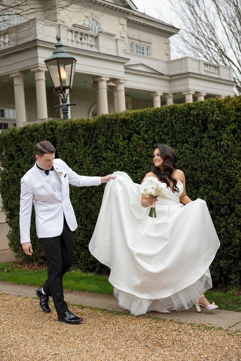 Groom holds bride's dress outside the Great Marsh Estate
