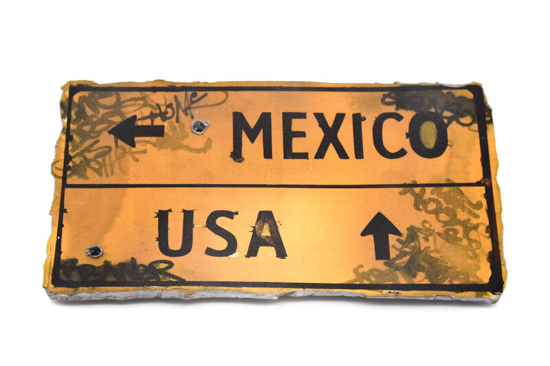 a yellow ceramic road sign has an arrow that points left to Mexico and forward to the USA.