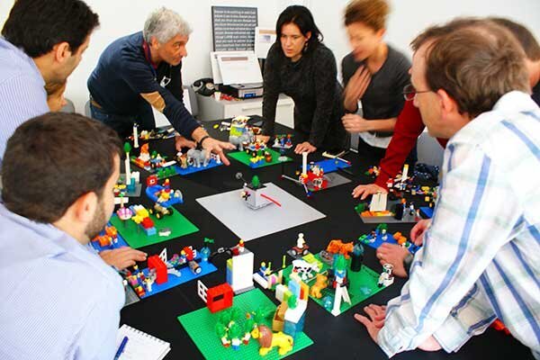 Men and women standing around a table filled with LEGO bricks at Shannon Russell's Lego Serious Play events. 