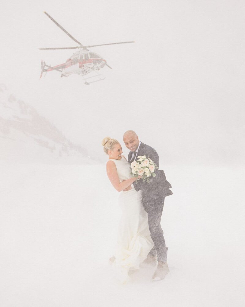 Capture the exhilarating moment of a bride and groom walking away from a helicopter as it takes off during their winter mountain wedding, with snow swirling around them. A breathtaking and adventurous scene of love and excitement.