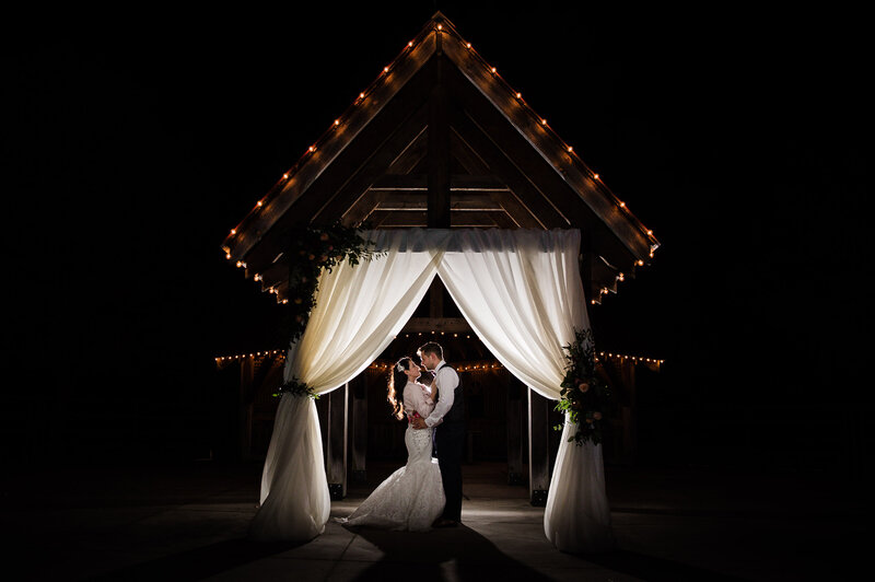 Bride and Groom facing and holding each other under arch - Night shot by Toronto Wedding photographer