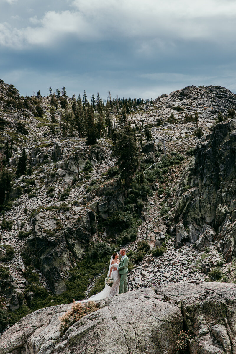 Bride and groom standing together on a rocky cliff surrounded by rugged granite peaks and evergreens during their adventurous Lake Tahoe elopement.