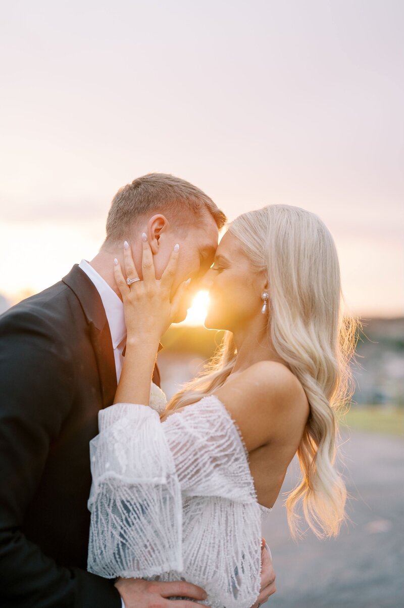 bride and groom kissing in front of the sunset