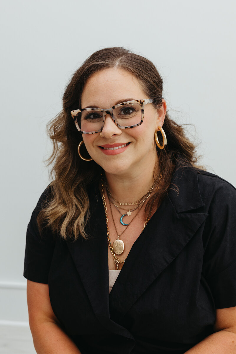 Woman in a black top and glasses with layered gold necklaces