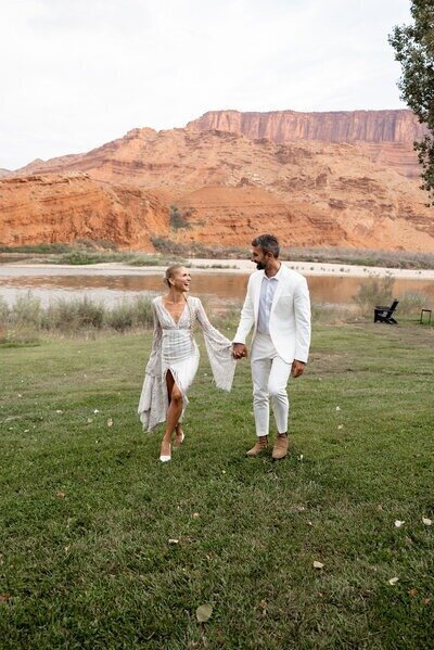 Couple walking and laughed with each other on green grass with beautiful moab river and mountains in background.