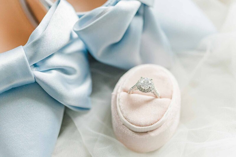 Blue satin wedding shoes arranged on white tulle with pink velvet ring box with diamond engagement  ring