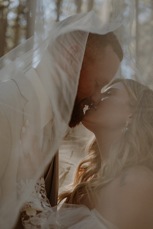 bride and groom kissing under veil at tenaya lake in yosemite