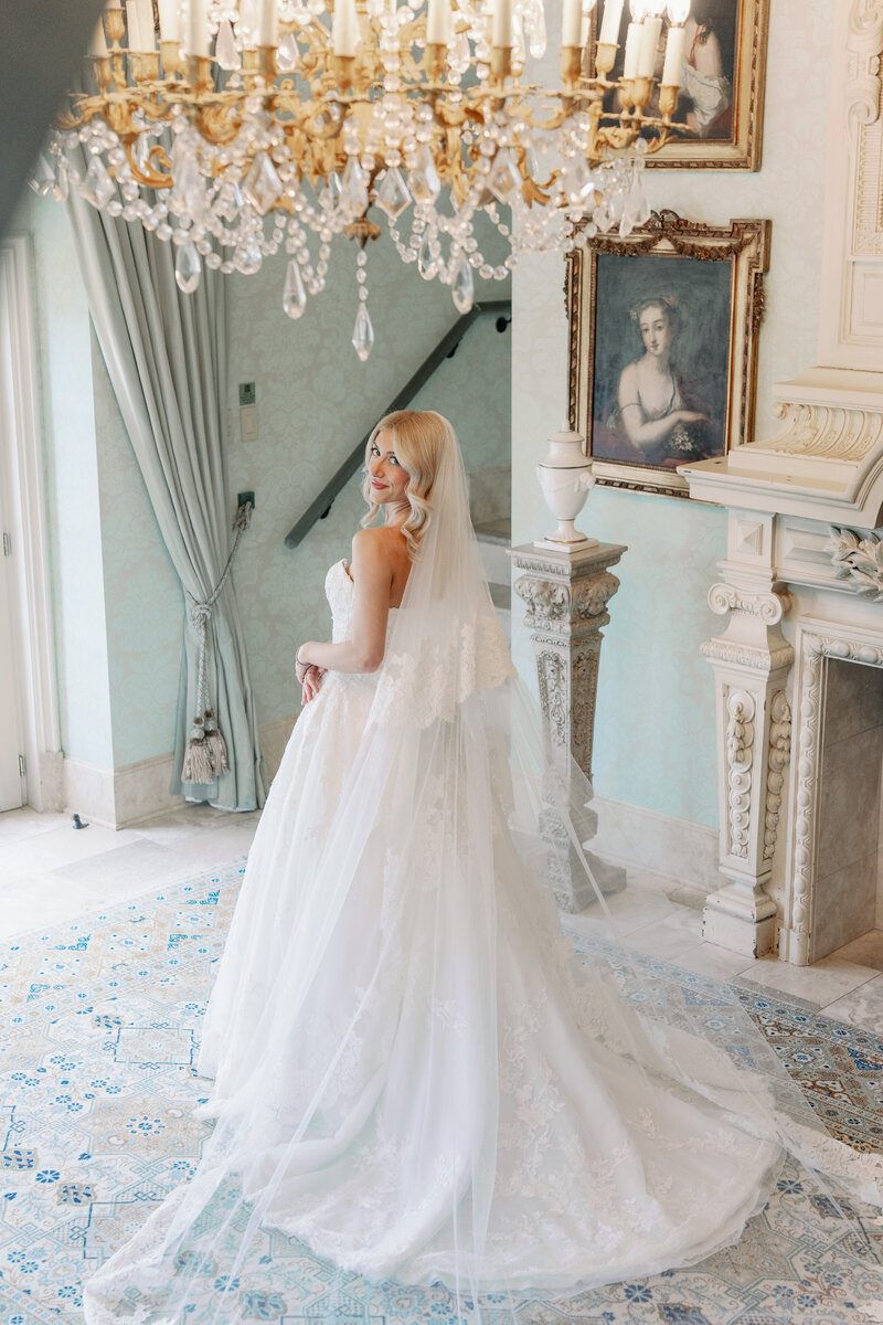 bride in wedding gown and long veil looking over her shoulder