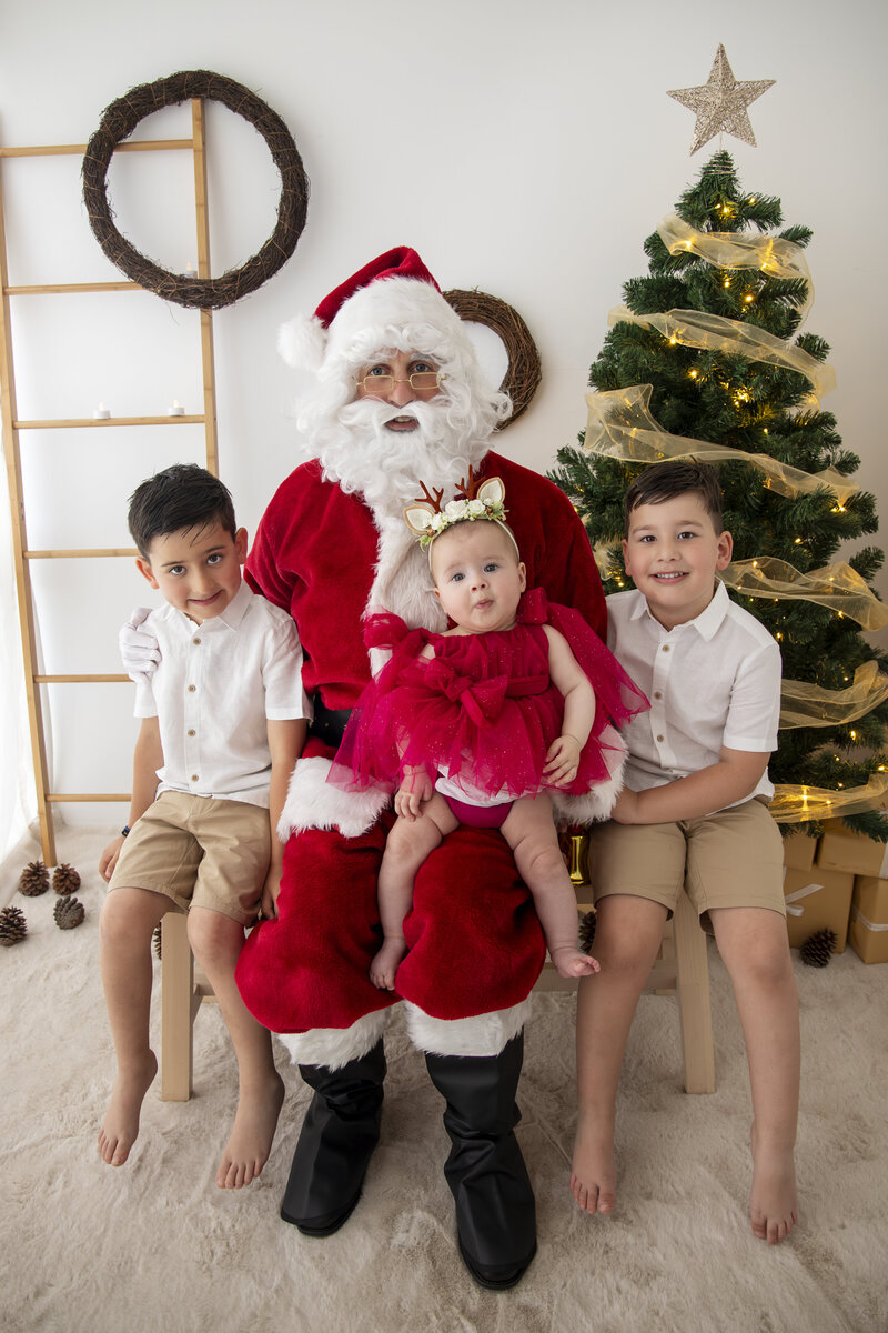 Children in Christmas minis session smiling in front of decorated Christmas tree