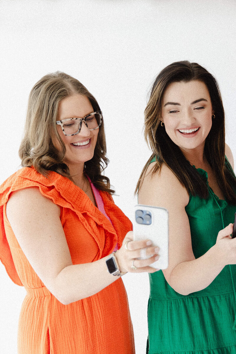 Two Women looking at a phone wearing bright colored dresses