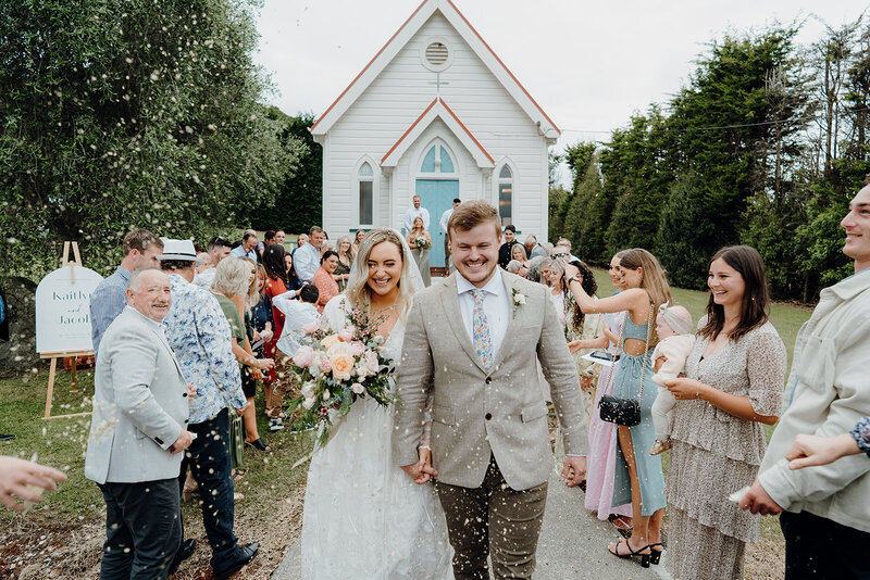 A newly married modern bride and groom  exiting the church while their guests throw confetti on them and photographed by Waikato Wedding Photographer Haley Adele