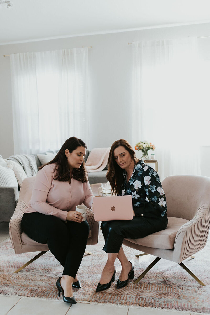 Idit and Yael sit together as they review something on a laptop screen. They offer couples therapy and marriage counseling in FL. Contact their practice for couples therapy in Florida, online couples counseling, and other services.