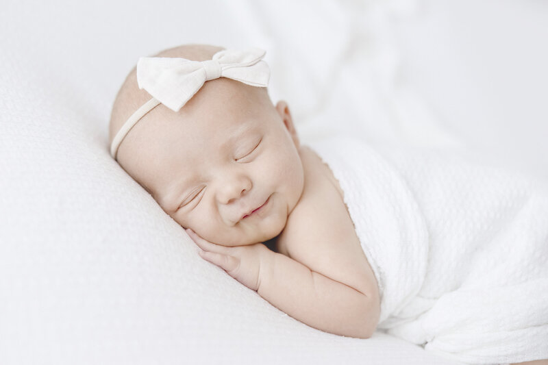 newborn baby sleeping on belly with white wrap and bow