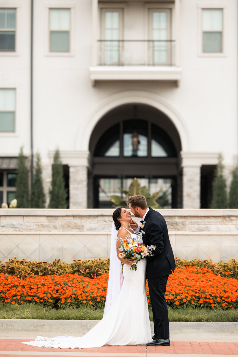 Bride smiling as groom kisses her cheek during joyful wedding portraits in Wichita Kansas