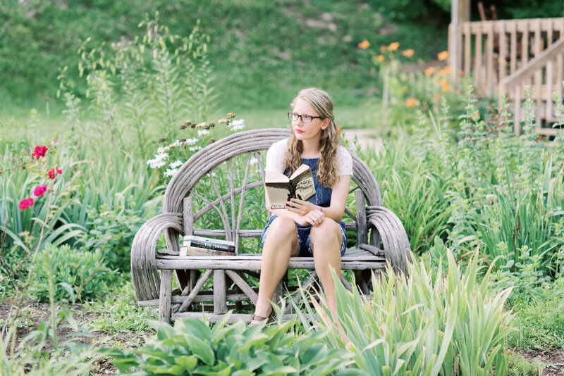 Girl sitting on a bench reading a book with tall grass around her